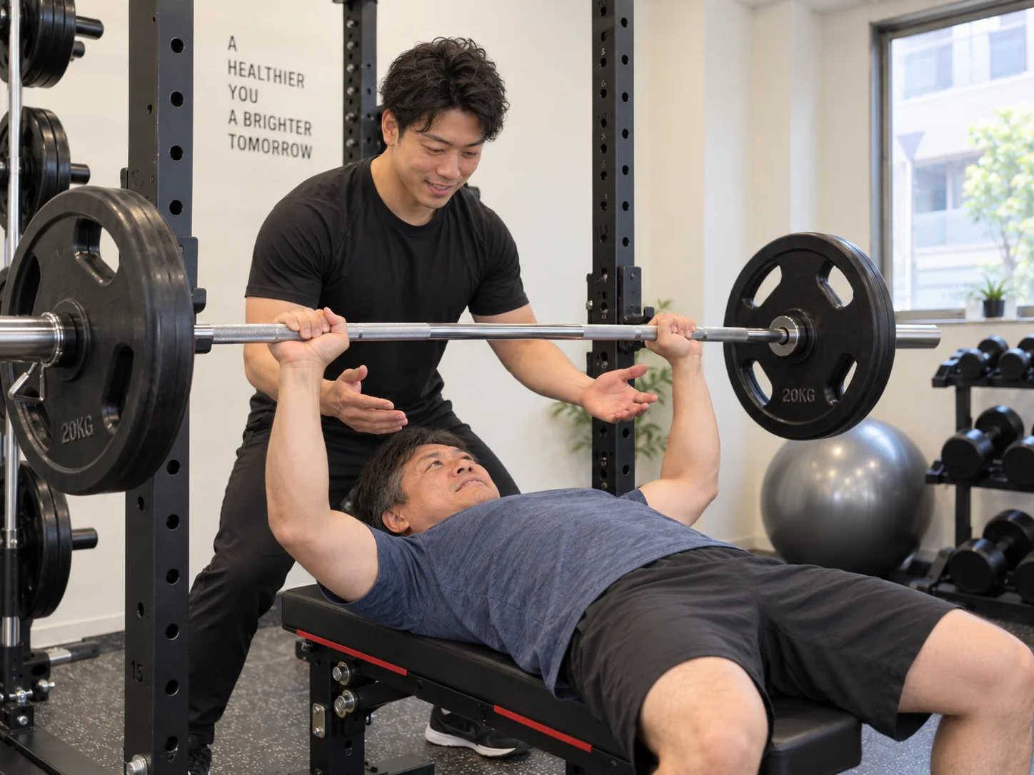 トレーナーのサポートを受けながらバーベルでベンチプレスをする様子